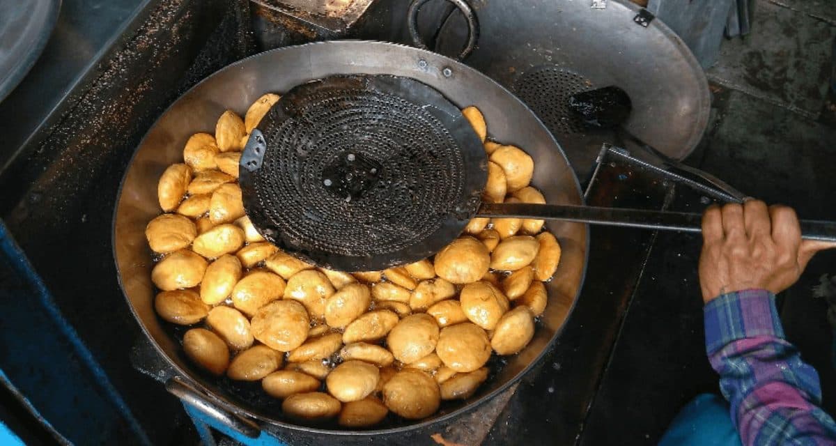 Golden kachoris deep-frying in a large kadai at a Jaipur street stall, being lifted out with a wire skimmer